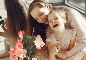 Mom hugging young daughter with flowers