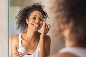 African American woman applying moisturizer to her face